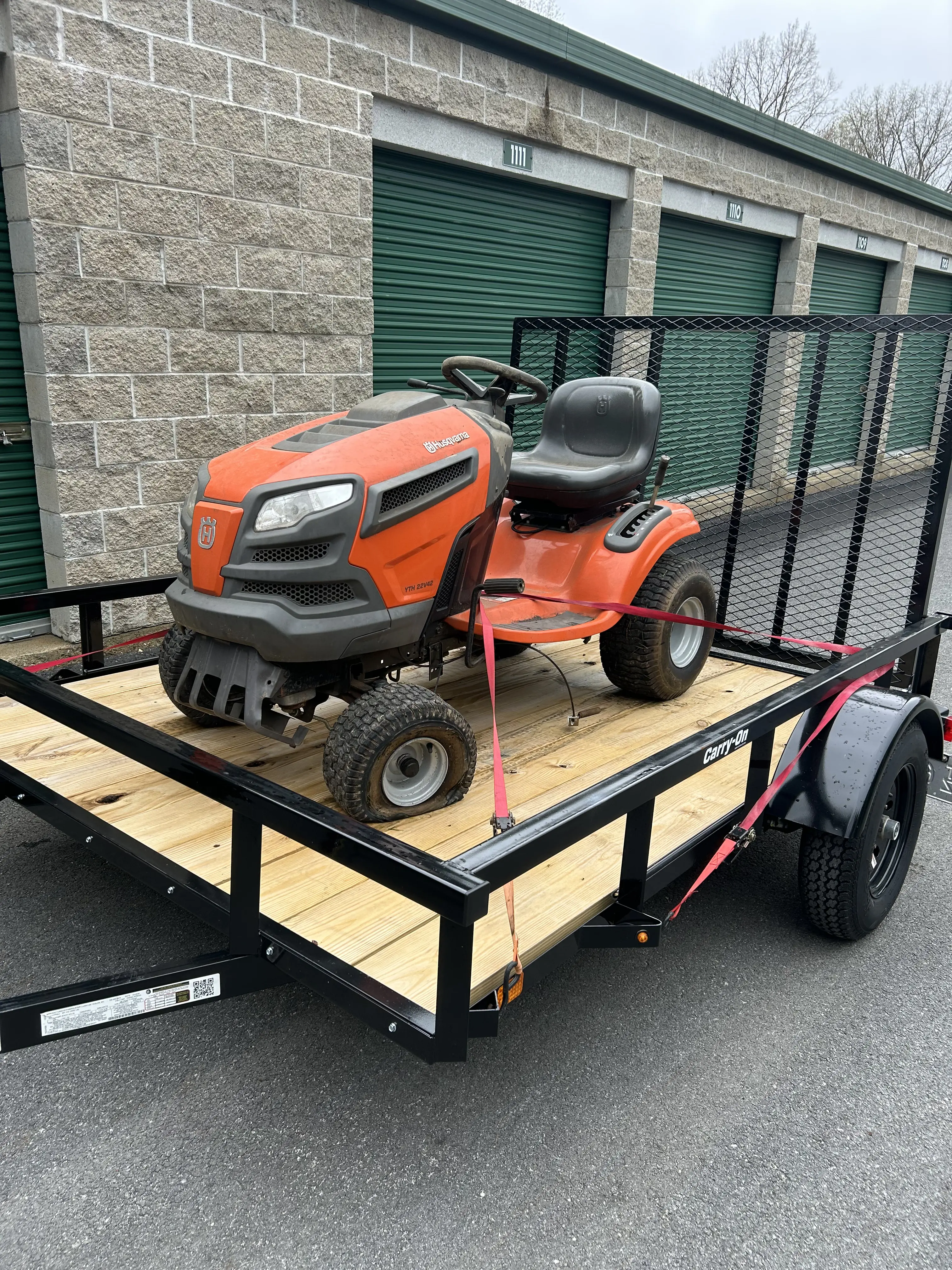 A lawn tractor strapped down on a flatbed trailer, ready to roll.